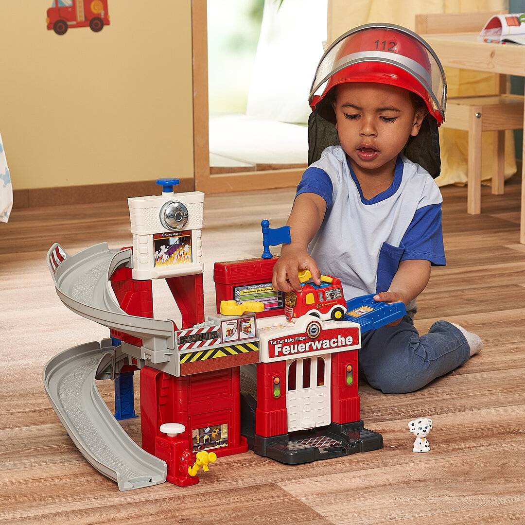 VTech Tut Tut Baby Flitzer Feuerwache, interaktives Spielgebäude ab 1 Jahr VTech Tut Tut Baby Flitzer Feuerwache aus Kunststoff mit 3 Liedern & 6 Melodien, 4 magischen Sensoren, Feuer-Spielstein, Löschschlauch, Hundefigur, kindersicher ab 1 J., Holz, Hartholz, Person, Helm, Gesicht